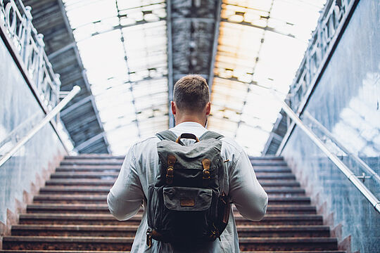Mann mit Rucksack von hinten geht Treppe zum Bahnhof hoch